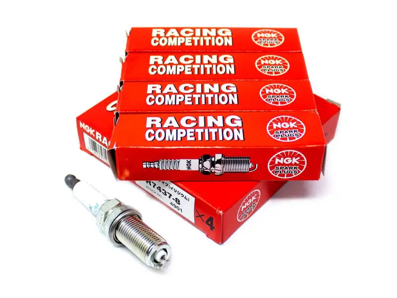 Four boxes of NGK Racing Competition spark plugs next to a single spark plug for the 7740 NGK Reg Plugs 4-Pack.