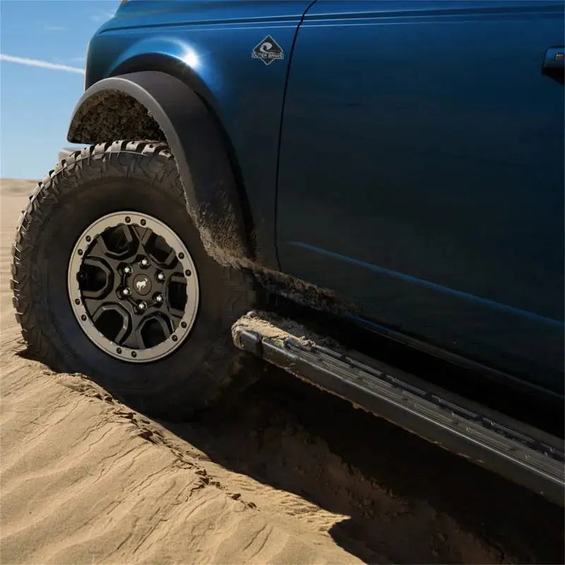 Ford Racing 21-22 Bronco Sasquatch Fender Flare Kit installed on a blue Ford Bronco, showcasing its rugged look and protection on sandy terrain.