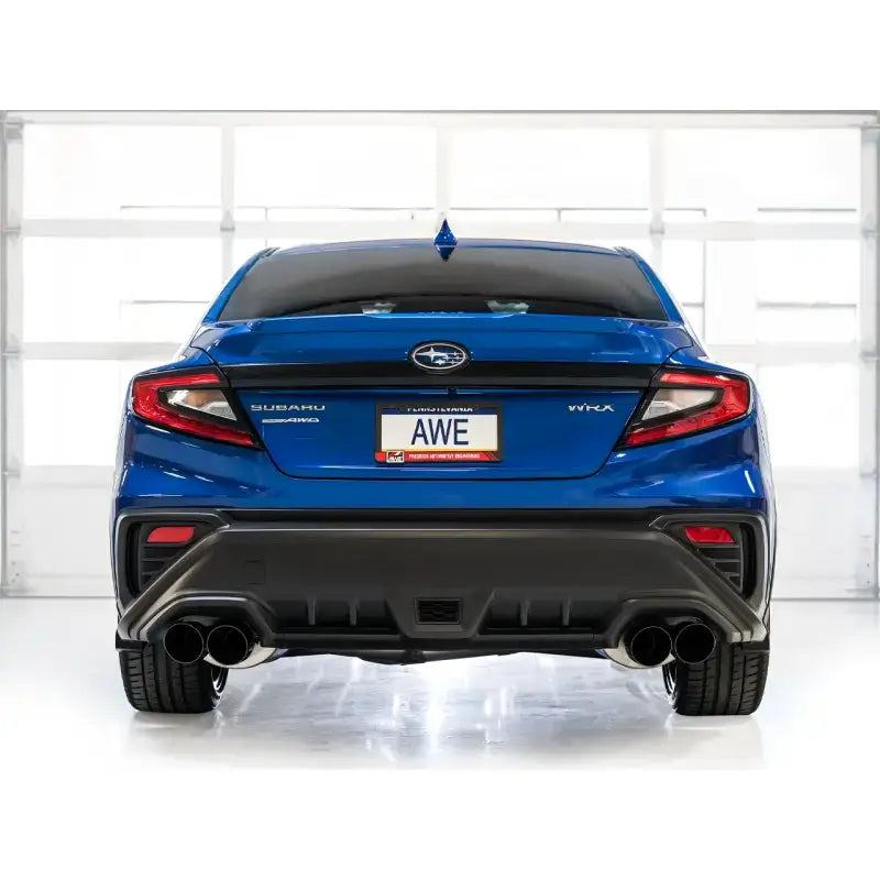 Blue Subaru WRX with AWE Track Exhaust displayed in a garage, showcasing dual exhaust pipes and AWE branding on the license plate.