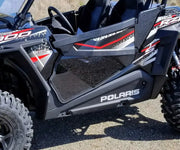 Black Polaris RZR with spike lower door and aggressive tires for off-road fun