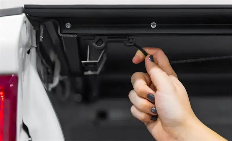 Person’s hand operating access lomax tri-fold cover latch on Ram 1500 truck bed