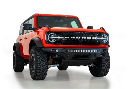 Addictive Desert Designs 2021+ Ford Bronco Stealth Fighter Front Bumper with Winch Mount in Hammer Black finish featuring a 30" radius light bar and cube light mounts, displayed on a red Ford Bronco.