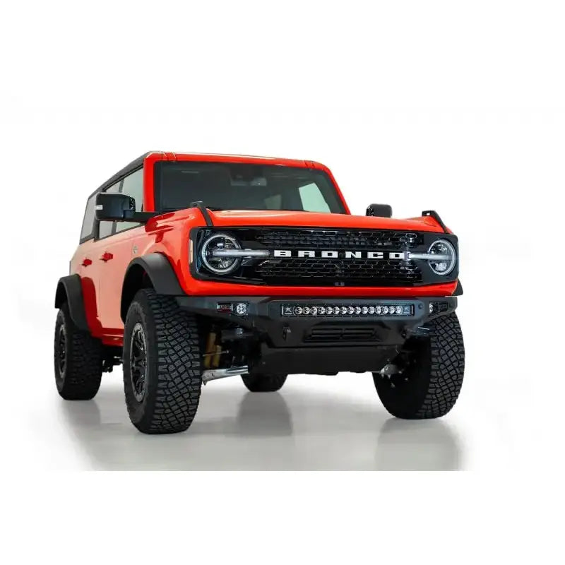 Addictive Desert Designs 2021+ Ford Bronco Stealth Fighter Front Bumper with Winch Mount in Hammer Black finish featuring a 30" radius light bar and cube light mounts, displayed on a red Ford Bronco.