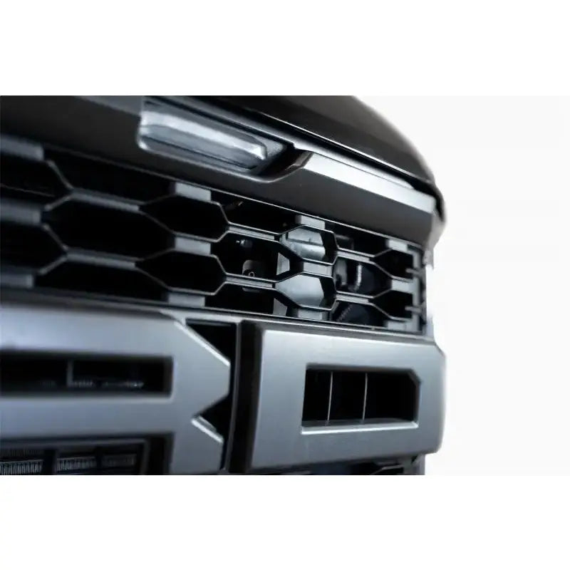 Close-up of Addictive Desert Designs Adaptive Cruise Control Relocation Bracket installed on a 21-22 Ford Raptor grille in Hammer Black.