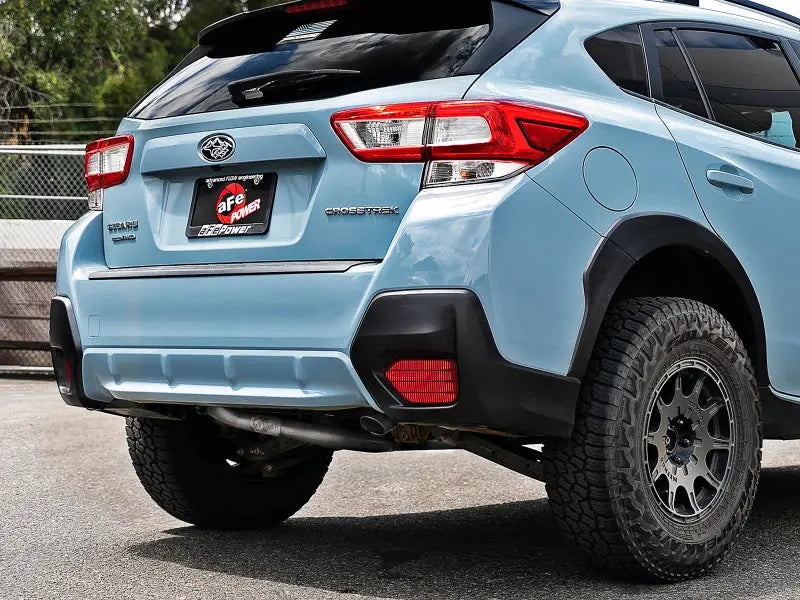 Rear view of a light blue Subaru Crosstrek (2018-2019) featuring the aFe POWER Takeda 2.5in 304 SS Cat-Back Exhaust System with rugged off-road tires.