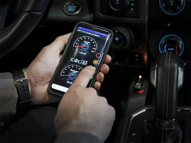 Black smartphone showing aFe Scorcher Blue dashboard app with speedometer