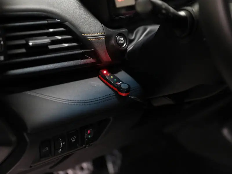 A compact, red and black electronic device with indicator lights, possibly for a vehicle’s dashboard.