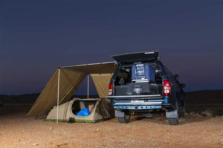 ARB Wind Break-Side setup with an awning for wind, sun, and rain protection, showing a camping scene by a vehicle at dusk.