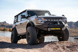 DV8 Offroad 2021+ Ford Bronco with Modular Front Bumper, Winch, and Auxiliary Light Mounts on rocky terrain with mountains in the background.