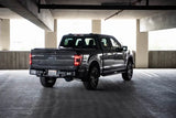 DV8 Offroad 21-23 Ford F-150 MTO Series Rear Bumper with steel construction and aluminum accents provides protection and utility steps, shown mounted on a gray Ford F-150 in a parking garage.