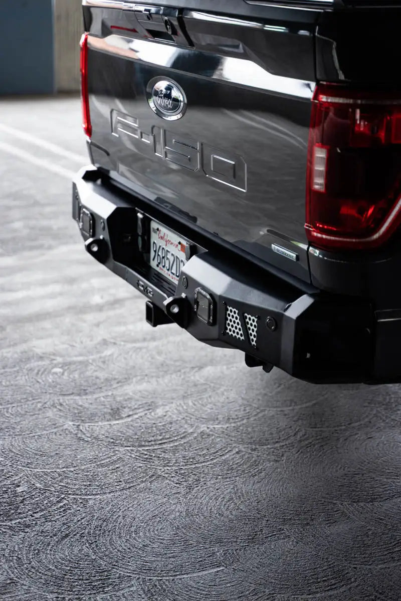 DV8 Offroad MTO Series Rear Bumper on a 2021-2023 Ford F-150, featuring gusseted steel construction, utility steps, and clevis mounts.