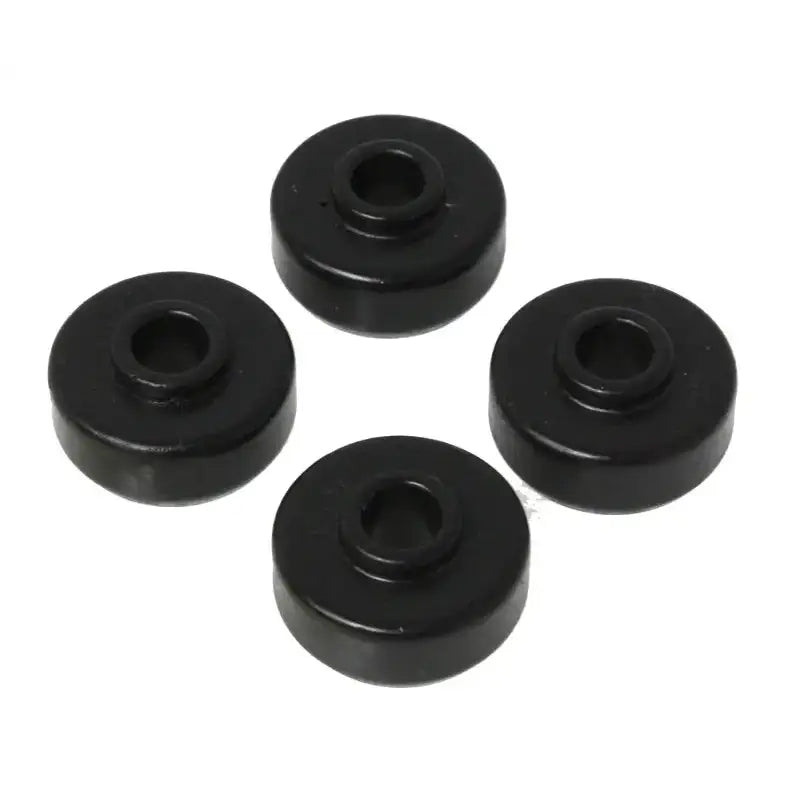 Four black, circular rubber grommets with central holes, arranged in a loose square pattern against a white background. Each grommet features a beveled edge and a cylindrical shape, forming the Energy Suspension Universal Black Shock Bushing Set by Energy Suspension.