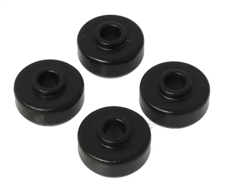 Four black, circular rubber grommets with central holes, arranged in a loose square pattern against a white background. Each grommet features a beveled edge and a cylindrical shape, forming the Energy Suspension Universal Black Shock Bushing Set by Energy Suspension.