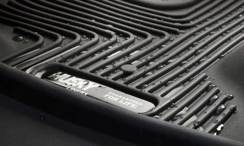 Husky Liners X-act Contour floor liner in black featuring raised ridge design and thermoplastic elastomer material with water droplets on the surface.