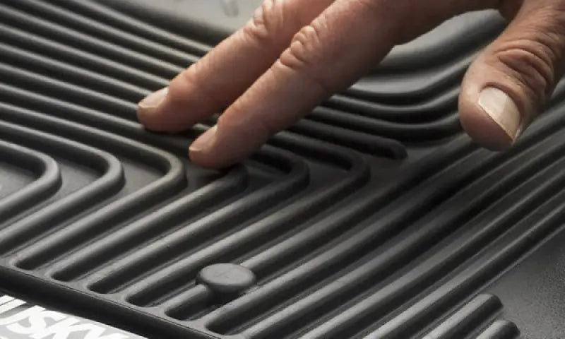 Husky Liners X-act Contour floor liner, molded-fit, raised ridge, black thermoplastic elastomer, close-up with hand touching textured surface.