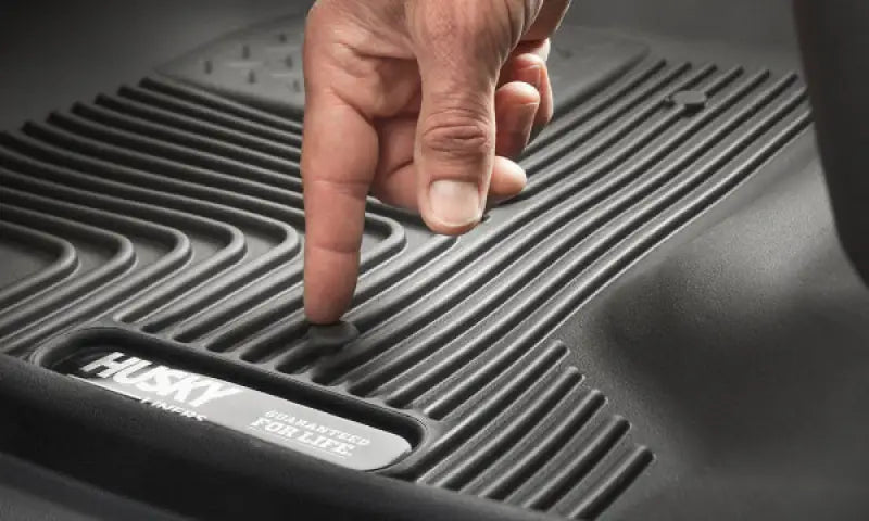 Husky Liners X-act Contour floor liner in black thermoplastic elastomer with molded fit and raised ridge, close-up of a hand pressing the rubberized material.