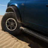 Ford Racing 21-22 Bronco Sasquatch Fender Flare Kit installed on a blue Ford Bronco, showcasing enhanced protection and rugged style. The vehicle is off-roading through sandy terrain.