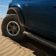 Ford Racing 21-22 Bronco Sasquatch Fender Flare Kit installed on a blue Ford Bronco, showcasing its rugged look and protection on sandy terrain.