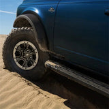 Ford Racing 21-22 Bronco Sasquatch Fender Flare Kit installed on a blue Ford Bronco, showcasing its rugged look and protection on sandy terrain.