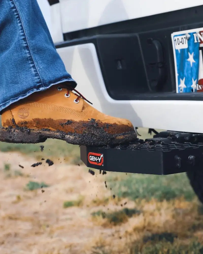 Mud-covered boot stepping on GH-030 Gen-Y Hitch with 2' shank, heavy-duty design, and serrated surface for secure towing connection.
