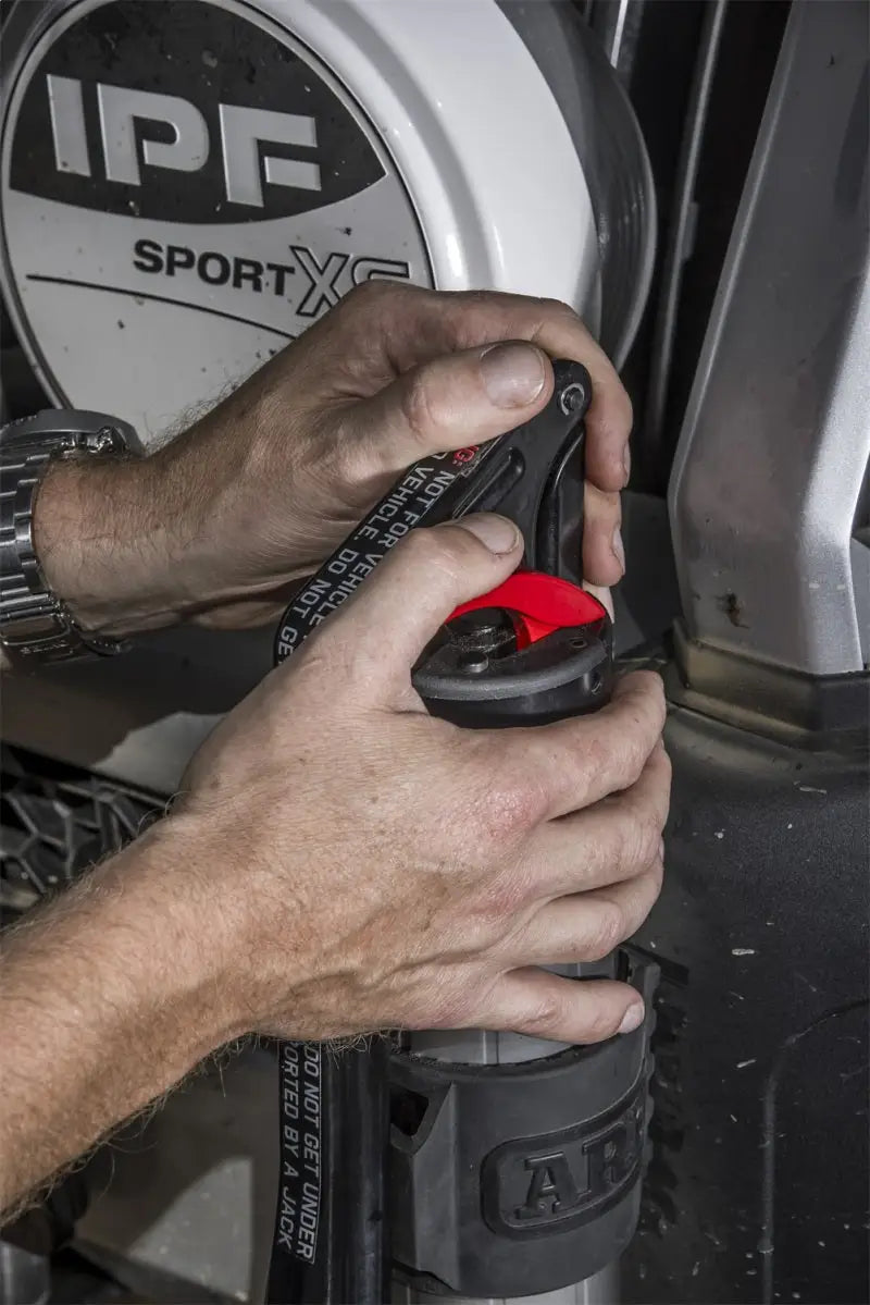 Hands operating the ARB hydraulic recovery jack with IPF lighting in the background.