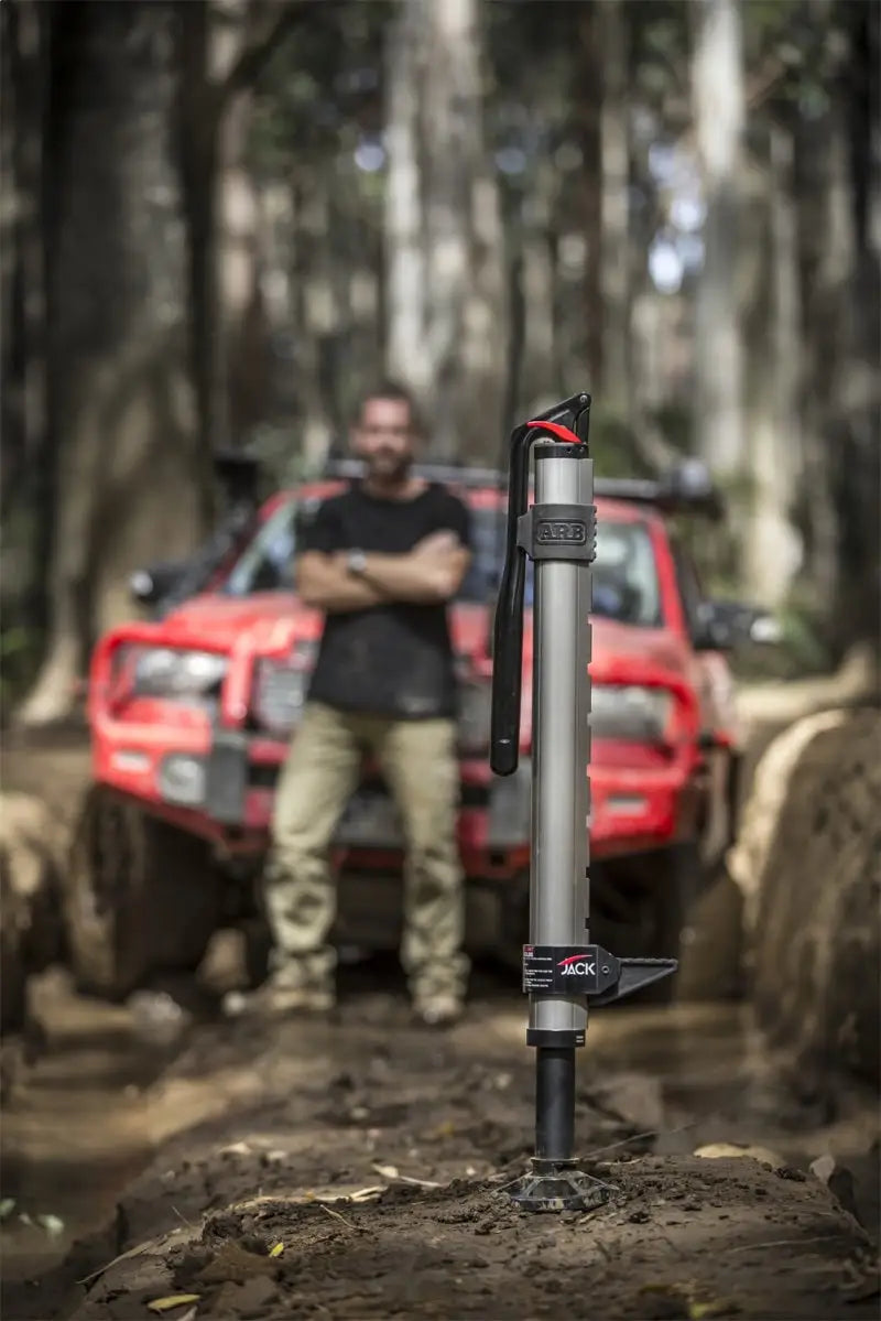 ARB Hydraulic Jack in outdoor setting with red off-road vehicle and person in background.
