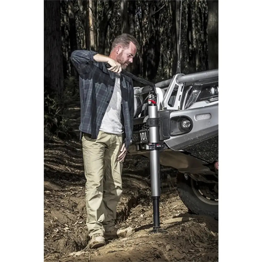 Man using ARB Hydraulic Jack to lift off-road vehicle in a forest setting.