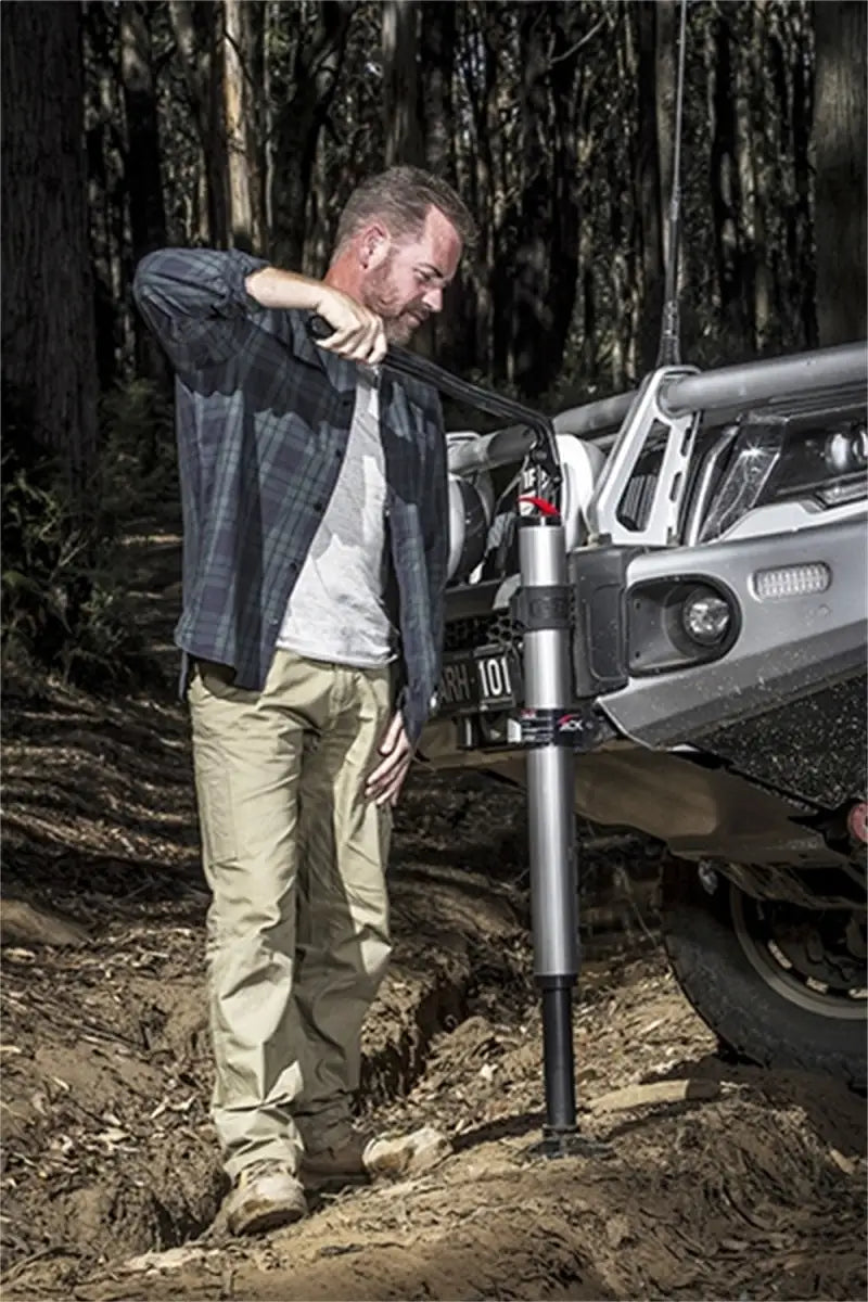 Man using ARB Hydraulic Jack to lift off-road vehicle in a forest setting.