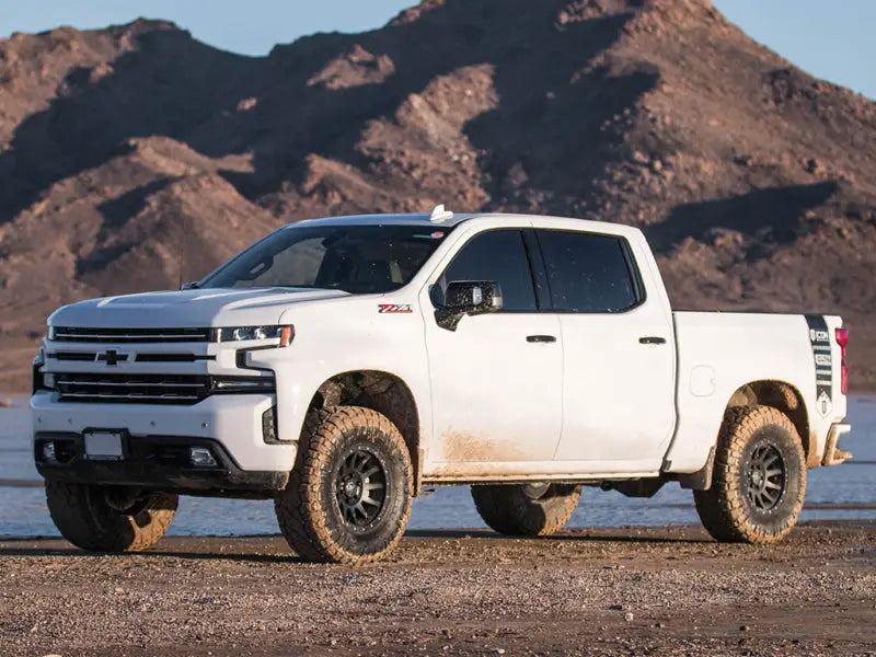 White Chevrolet truck with off-road tires featuring the ICON 2019+ GM 1500 1.5-3.5in Stage 4 Suspension System with Billet UCA in a rugged desert landscape.