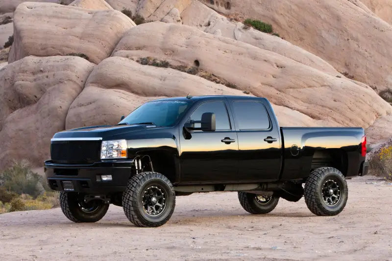 Black pickup truck equipped with K1046DL Fabtech Lift Kit Suspension driving through rugged desert terrain, showcasing enhanced off-road capability and aggressive stance.