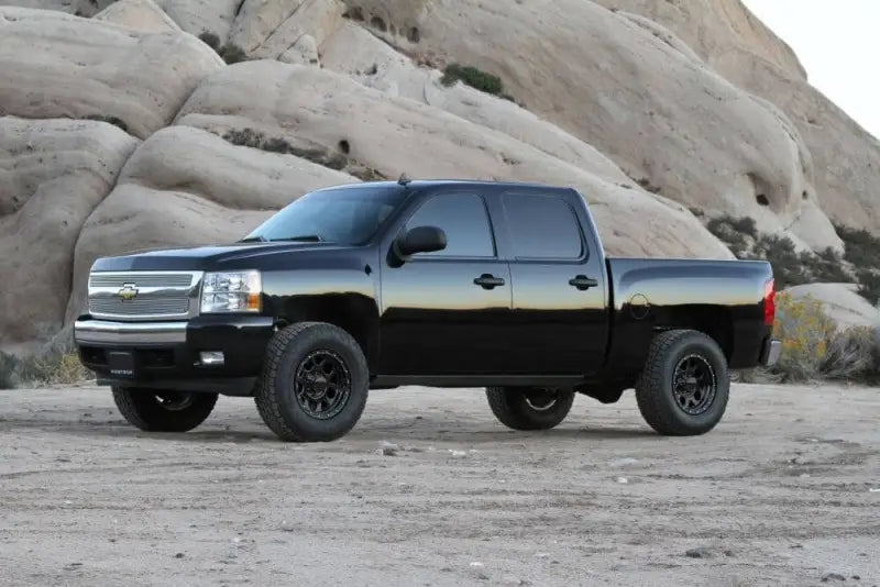 K1059 Fabtech Lift Kit Suspension installed on black Chevrolet Silverado, off-road in rocky desert terrain.