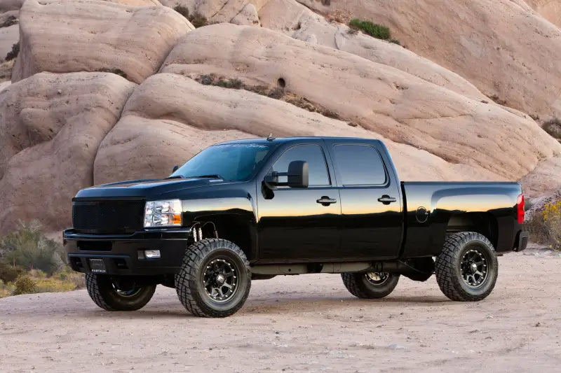 Black pickup truck equipped with K1065DL Fabtech Leveling Kit Suspension, enhancing stance and ground clearance, parked in a rocky desert landscape.