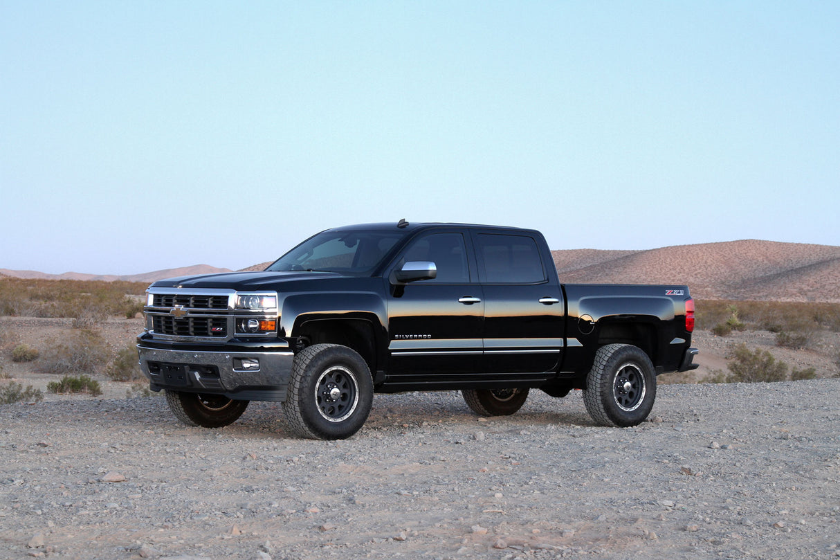 Black truck with significant lift featuring the K1070DL Fabtech Lift Kit Suspension, parked on rough desert terrain.