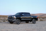 Black truck with significant lift featuring the K1070DL Fabtech Lift Kit Suspension, parked on rough desert terrain.
