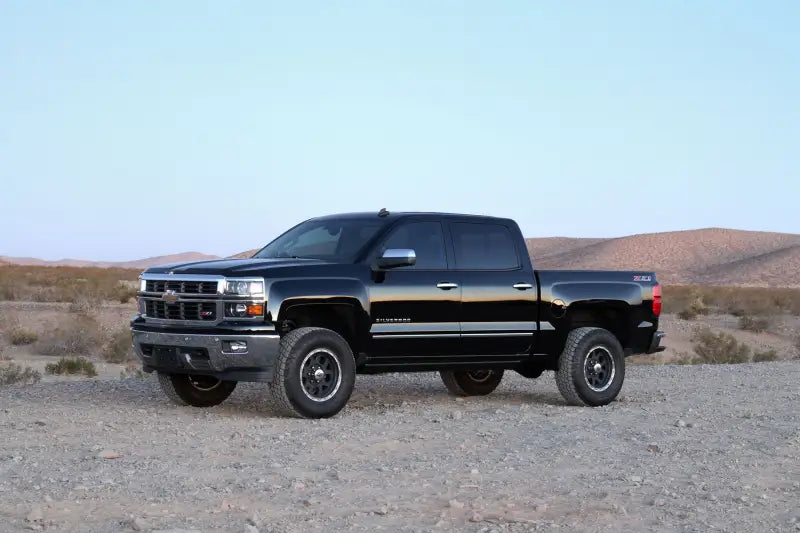 Black truck with significant lift featuring the K1070DL Fabtech Lift Kit Suspension, parked on rough desert terrain.