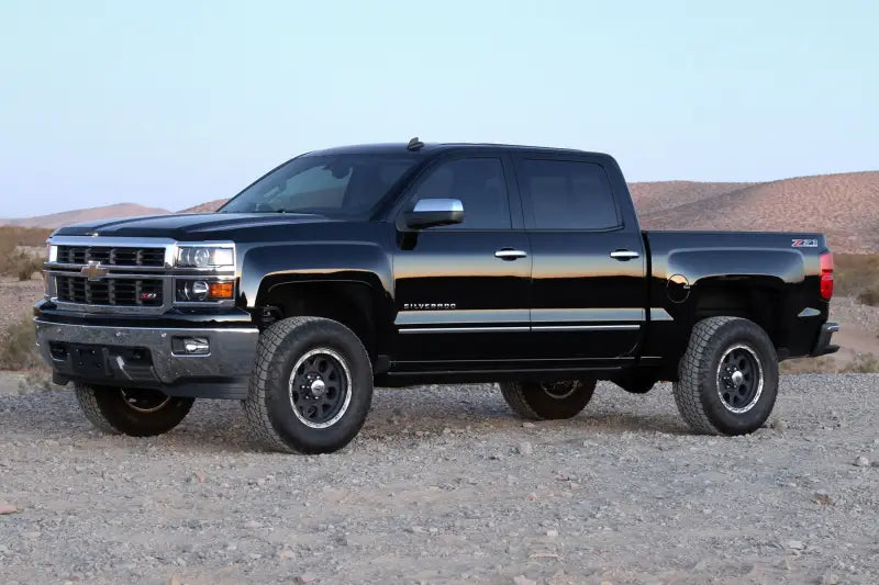 Black Chevy Silverado truck with K1071DL Fabtech Lift Kit Suspension parked in a desert landscape, showcasing enhanced ground clearance and off-road capability.