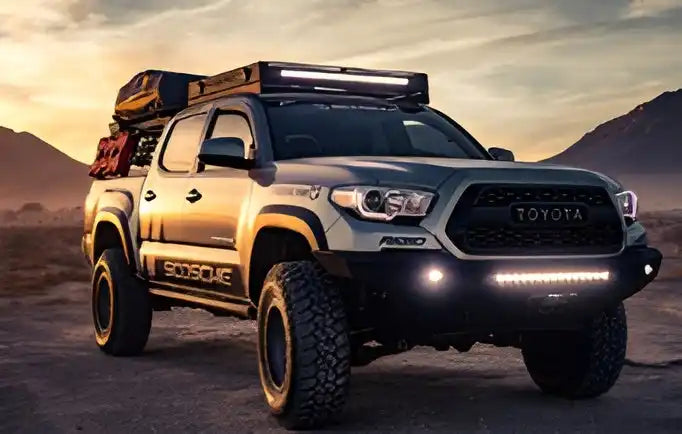 A lifted gray Toyota Tacoma pickup truck, equipped for off-road adventures with a roof rack, rooftop tent, and auxiliary lighting.