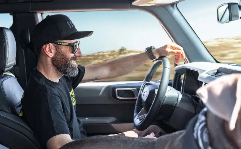 Man driving and smiling inside a car, representing the experience of using a MagnaFlow Muffler Mag SS 14X4X9 2.5 D/D for enhanced performance and sound.