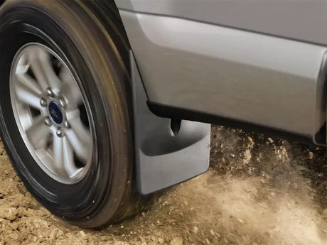Black thermoplastic mud flap without logo fits snugly behind vehicle tire, featuring WeatherTech QuickTurn Fastening System, protecting against dirt and debris.