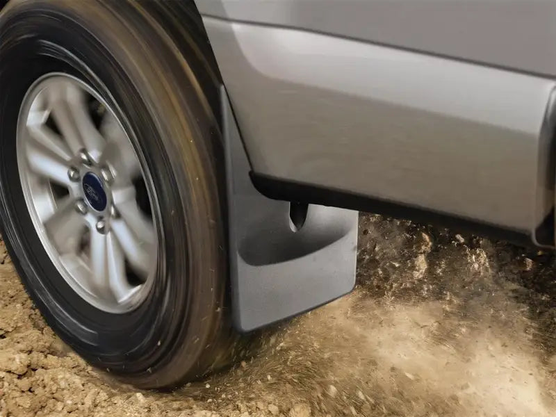 Black thermoplastic mud flap without logo fits snugly behind vehicle tire, featuring WeatherTech QuickTurn Fastening System, protecting against dirt and debris.