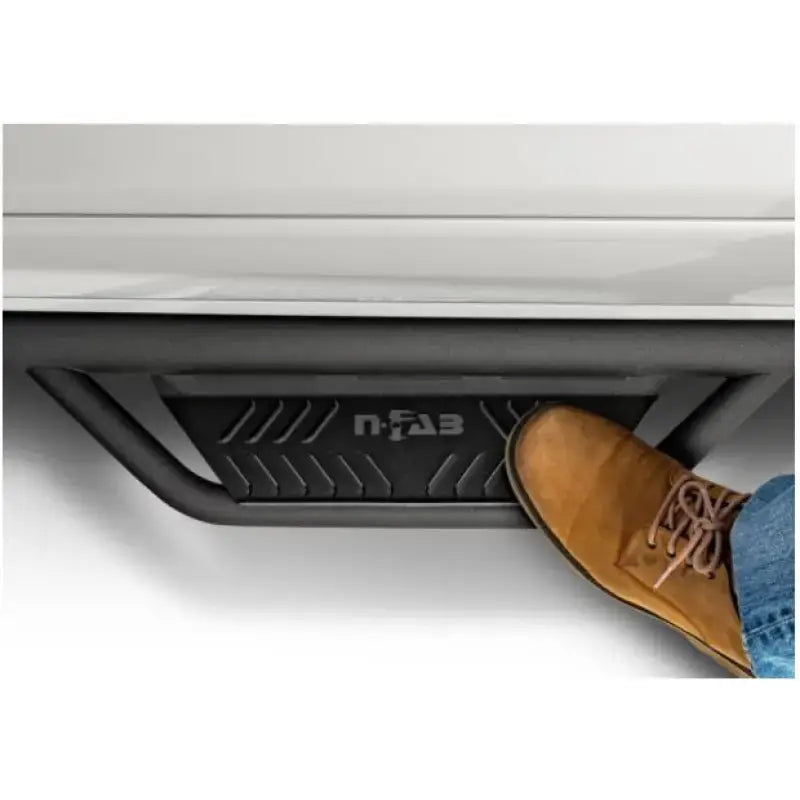 Black stainless steel nerf bar with drop down steps and a tan shoe on it