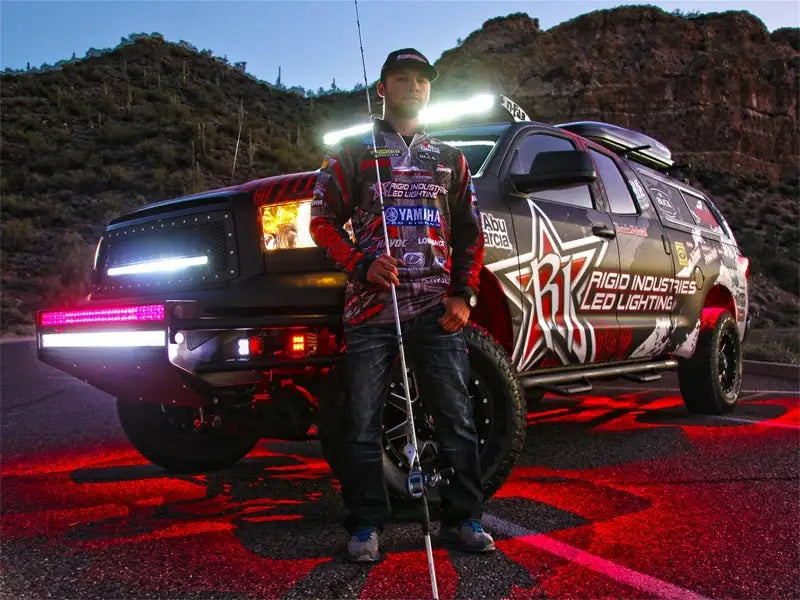 Man standing near off-road truck illuminated by Rigid Industries Rock Light Kit - Cool White, showcasing vibrant, strategic LED lighting for enhanced night visibility.