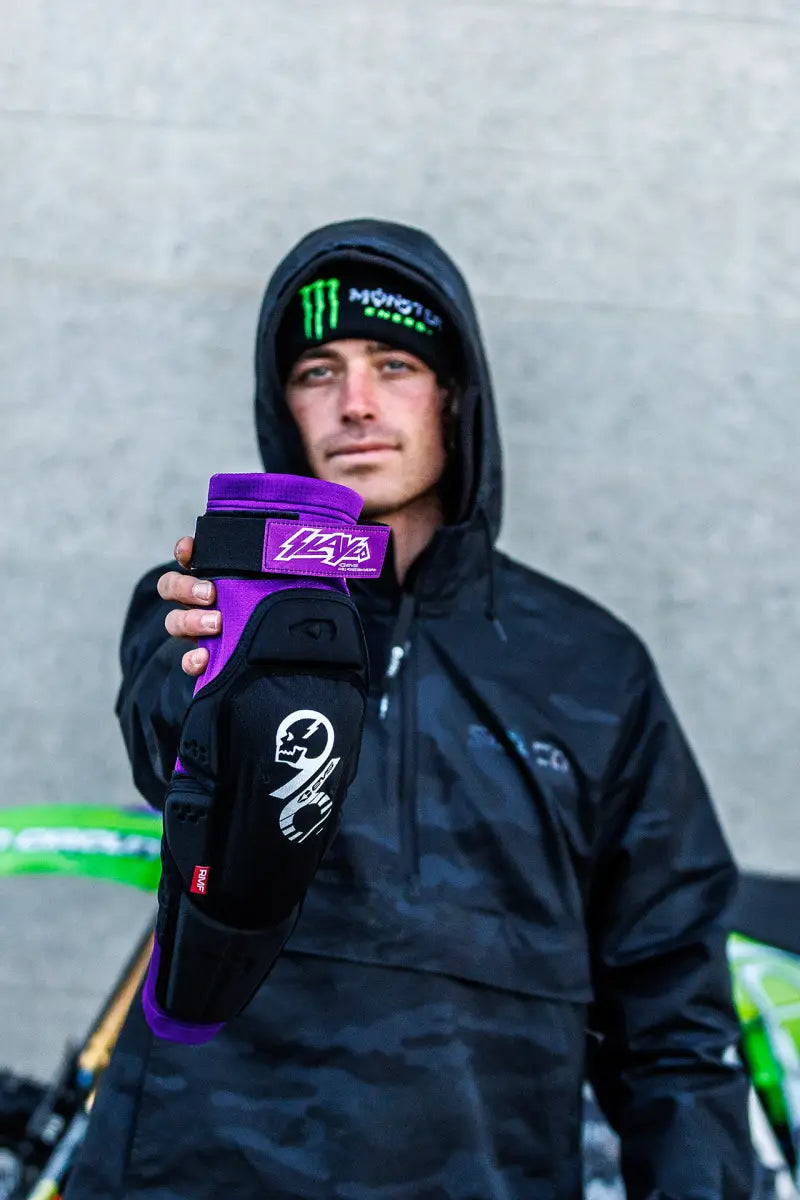 SLAY96K-L/X Slayco96 Knee Pad Lg/Xl being held up by a person wearing a black hooded jacket and a beanie.