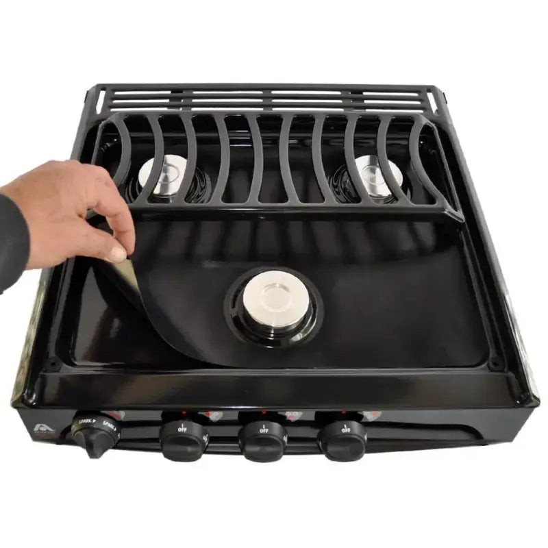 SWRV300 Stove Wrap Stove Top Protectors for Atwood/Dometic stoves, showing a hand lifting the protector to reveal the stove surface underneath.
